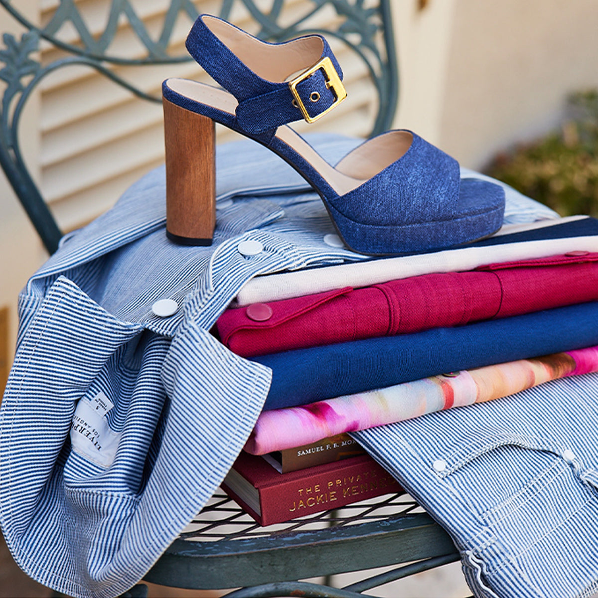 Stack of colorful clothes with denim high heel sandal on chair.