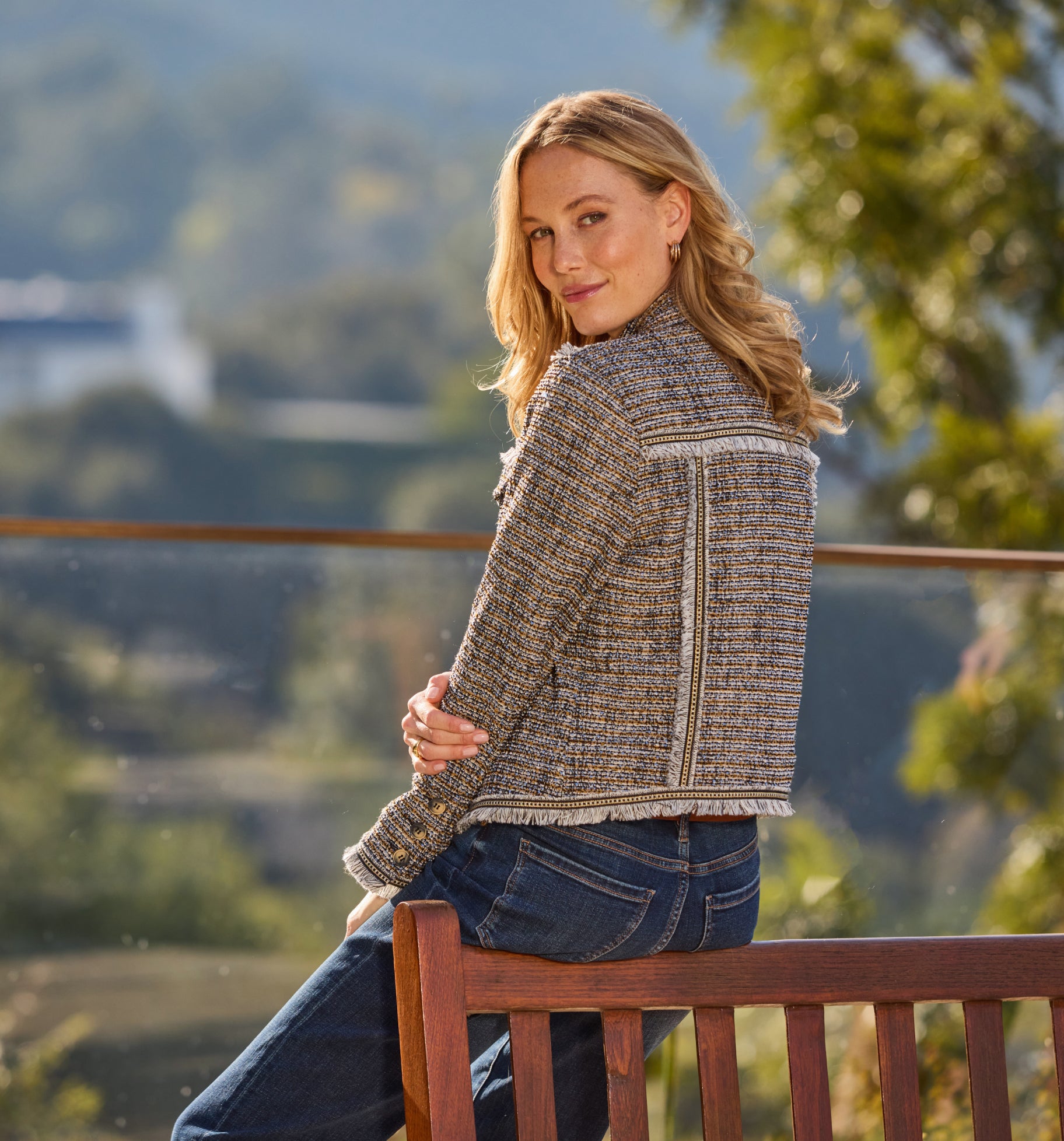 Blonde woman sitting on bench in tweed jacket outdoors