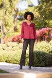 Woman in stylish red patterned blouse and black flared pants outdoors.